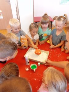 Na zdjęciu dzieci wsypujące mąkę do dużego pojemnika.