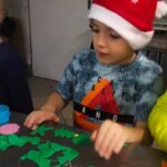 Chłopiec w czapce Mikołaja pokazuje swoje przygotowane ozdoby z zielonej masy cukrowej.