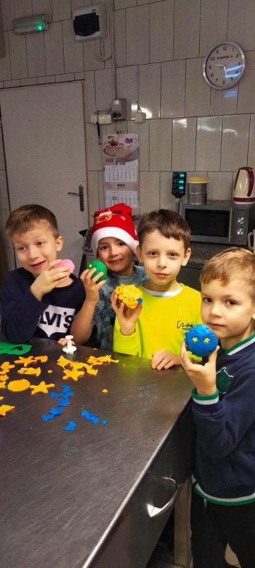 Czterech chłopców ( chopiec w bluzie z białym napisem, chłopiec w czapce Mikołaja, chłopiec w limonkowej bluzie oraz chopiec w bluzie z zielonymi wstawkami) w swoich rączkach pokazują ukończone ciasteczko piernikowe.