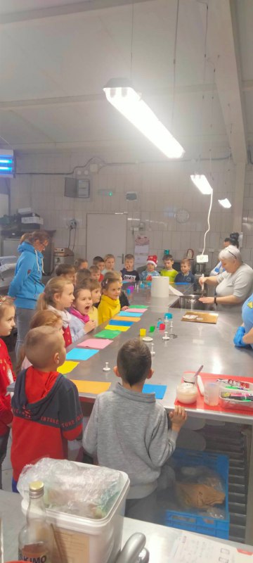 Uczniowie klasy zgromadzenie wokół prostokątnego stołu z kolorowymi kawałkami masy cukrowej w dekoratorni tortów.