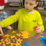 Chłopiec w limonkowej bluzie układa swoje ozdoby z pomarańczowej masy cukrowej.