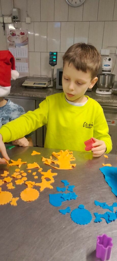 Chłopiec w limonkowej bluzie układa swoje ozdoby z pomarańczowej masy cukrowej.