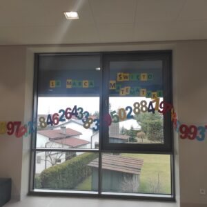Dekracja szkolnego korytarza, na oknie rozwieszone kolorowe rozwinięcie liczby pi