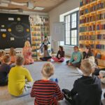 Dzieci siedzą w kręgu na dywanie wraz z biblitekarzem