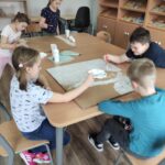 Dzieci, siedzące przy stole, malują tekturę białą farbą