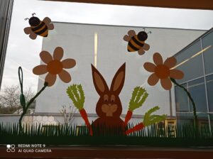 Dekoracja okienna. Duże stokrotki, królik, pszczoły, trawa, naklejone na szybie.