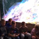 grupa dzieci na tle podświetlonego plakatu kosmosu. m