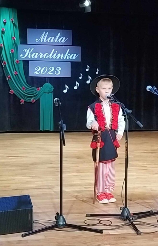 Jakub na scenie - w śląsko- góralskim stroju- w tle widać napis: Mała Karolinka 2023